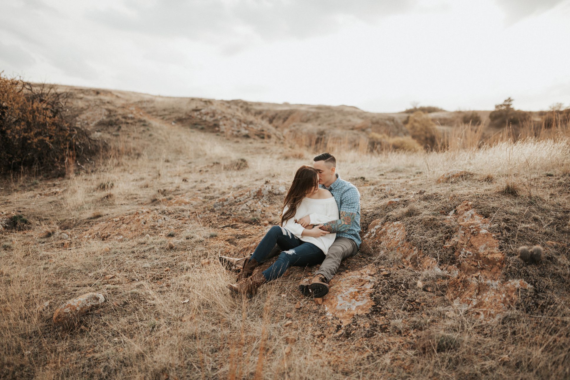 A girl sitting between her fiancé's legs at their Wichita Mountain engagement session. 