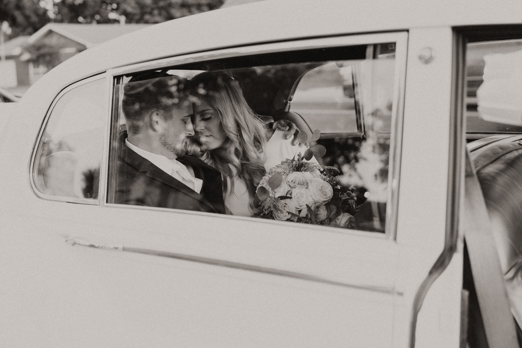 A bride and groom sitting in a Rolls Royce car on their wedding day.